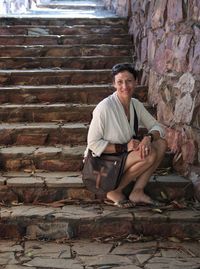 Full length portrait of smiling woman sitting on staircase