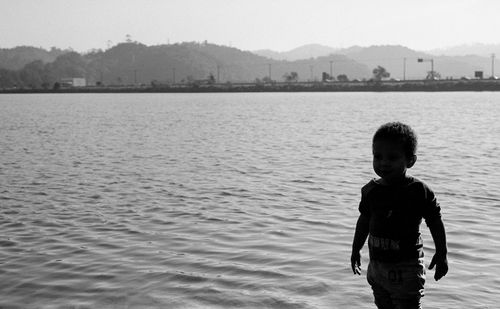 Silhouette boy standing by sea against clear sky