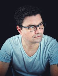 Serious man wearing eyeglasses looking away while sitting against black background