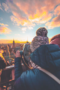 Woman looking through coin-operated binoculars against sky during sunset