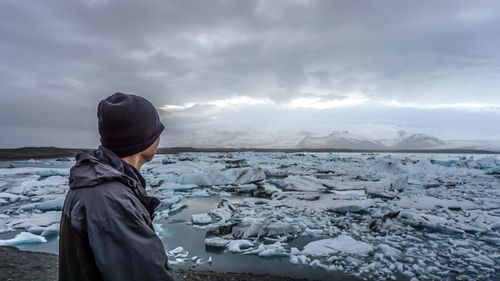 Man looking away while standing by lake against sky during winter