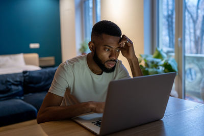 Focused african american guy freelancer working on laptop at home office, feeling overwhelmed