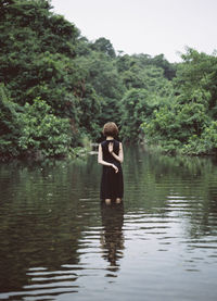 Rear view of woman standing in lake against trees