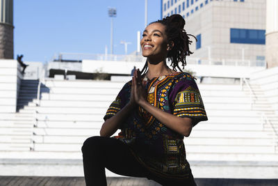 Smiling young woman looking away while standing against wall