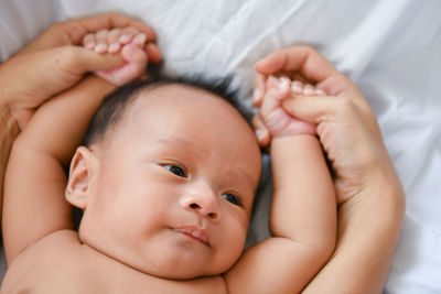 Cropped hands of mother holding shirtless toddler son on bed