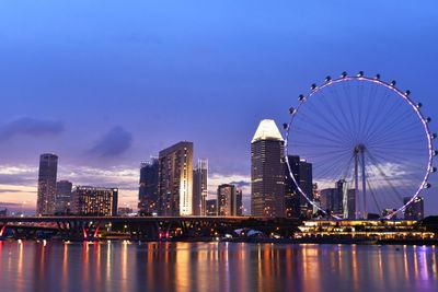 Illuminated ferris wheel in city against sky