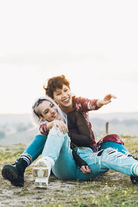 Young couple sitting on woman against sky