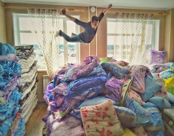 Happy man jumping over heap of mattresses against window