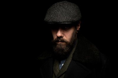Dark portrait of a bearded male in 1920 style clothing wearing a paper boy cap covering his eyes