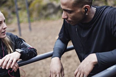 Sporty couple talking while leaning on parallel bars in forest