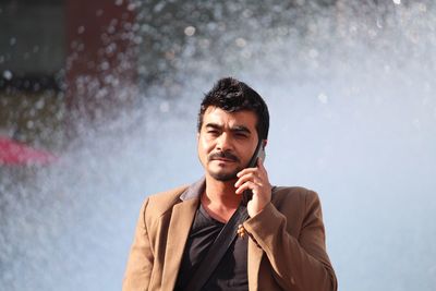 Portrait of young man talking on mobile phone while standing against fountain