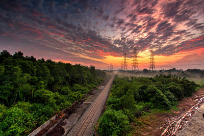 Railroad track amidst trees against sky during sunset