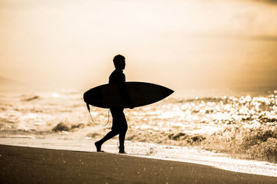 Silhouette of surfer on beach against sky during sunset