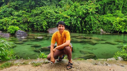 Portrait of man sitting by lake against trees