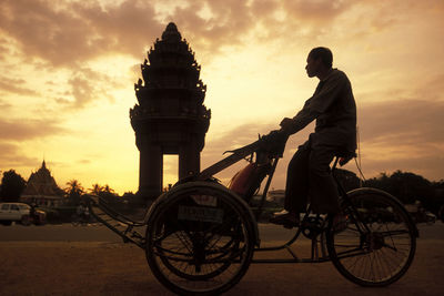 Man riding bicycle against sky during sunset