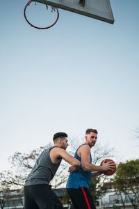 Low angle view of men playing with basketball against clear sky