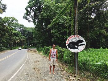 Woman standing by road against trees