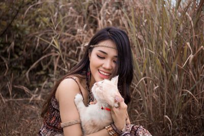 Smiling woman with cat sitting on field