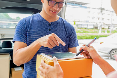 Cropped hands of woman signing in digital tablet while delivery man pointing