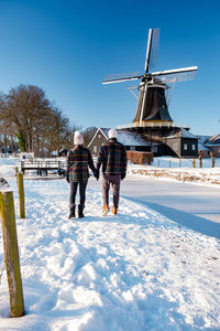 Rear view of people walking on snow covered field