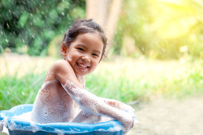 Portrait of happy girl taking bath in backyard