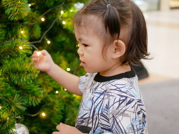 Side view of cute baby girl standing by christmas tree at home