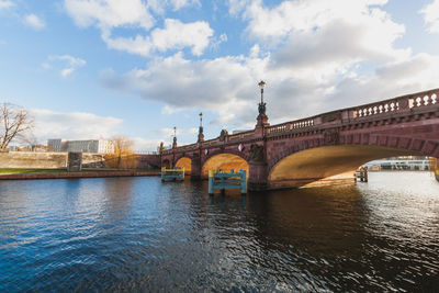 Arch bridge over river against cloudy sky