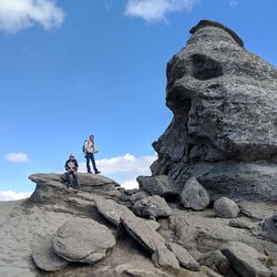 Low angle view of hikers on rock formation against blue sky