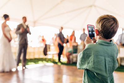 Rear view of boy photographing wedding ceremony on mobile phone