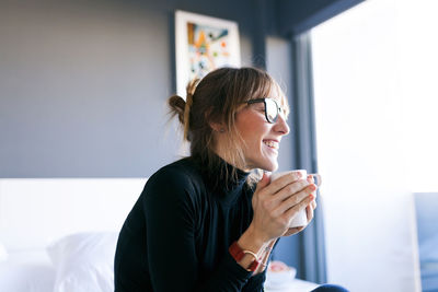 Happy young woman at home drinking cup of coffee