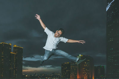 Playful man jumping against illuminated city at dusk