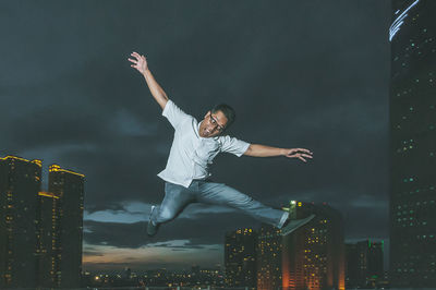 Full length of man jumping in city against sky at night