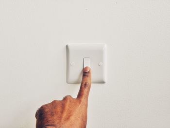 Cropped hand of man pressing switch board against wall