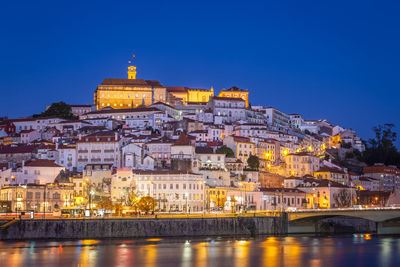 Illuminated buildings by river against sky in city at night