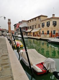 Boats moored in canal by buildings against sky
