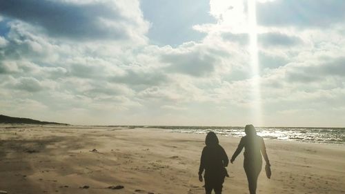 Rear view of couple standing on beach against sky