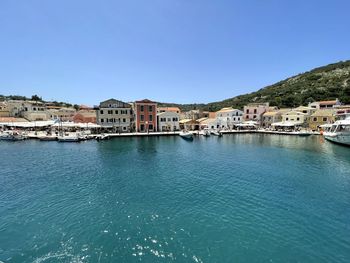 Buildings by sea against clear blue sky