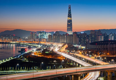 Light trails on road amidst buildings against sky at night