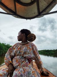 Black woman in a colorful flowery dress and rides at the front of a boat on lake nanga.