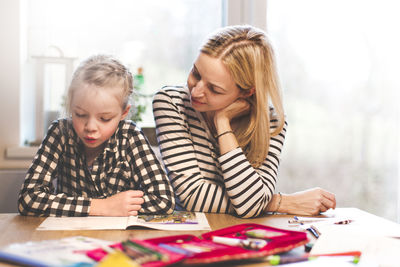 Girl studying while sitting with mother at home