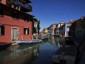 Boats moored on canal amidst buildings against sky