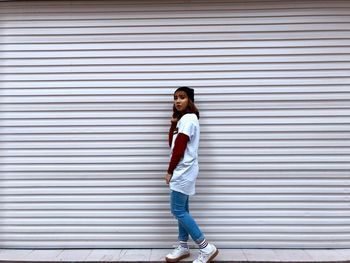 Full length of young woman standing on sidewalk by wall