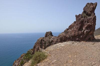 Rock formations by sea against clear sky