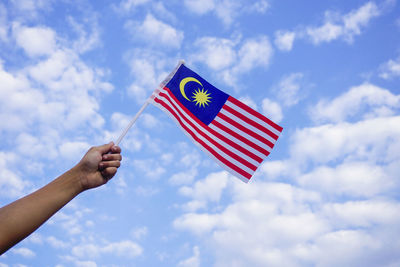 Low angle view of hand holding flag against sky