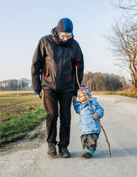 Grandfather and granddaughter walking on dirt road during winter