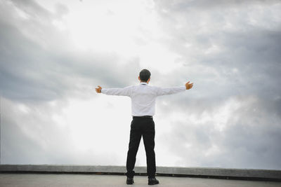 Man with arms outstretched standing against cloudy sky