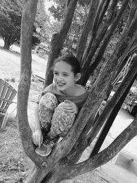 Tilt shot of happy girl sitting on tree trunk at park