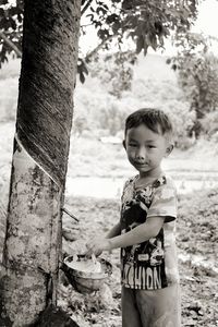 Portrait of boy collecting latex falling from tree trunk