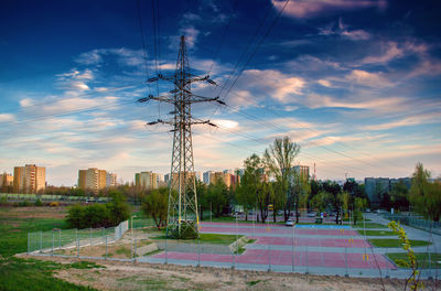 Electricity pylon by trees against sky during sunset