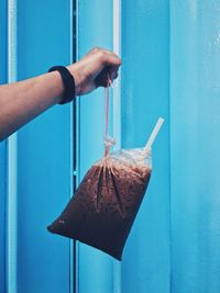 Cropped hand holding smoothie in plastic bag against wall